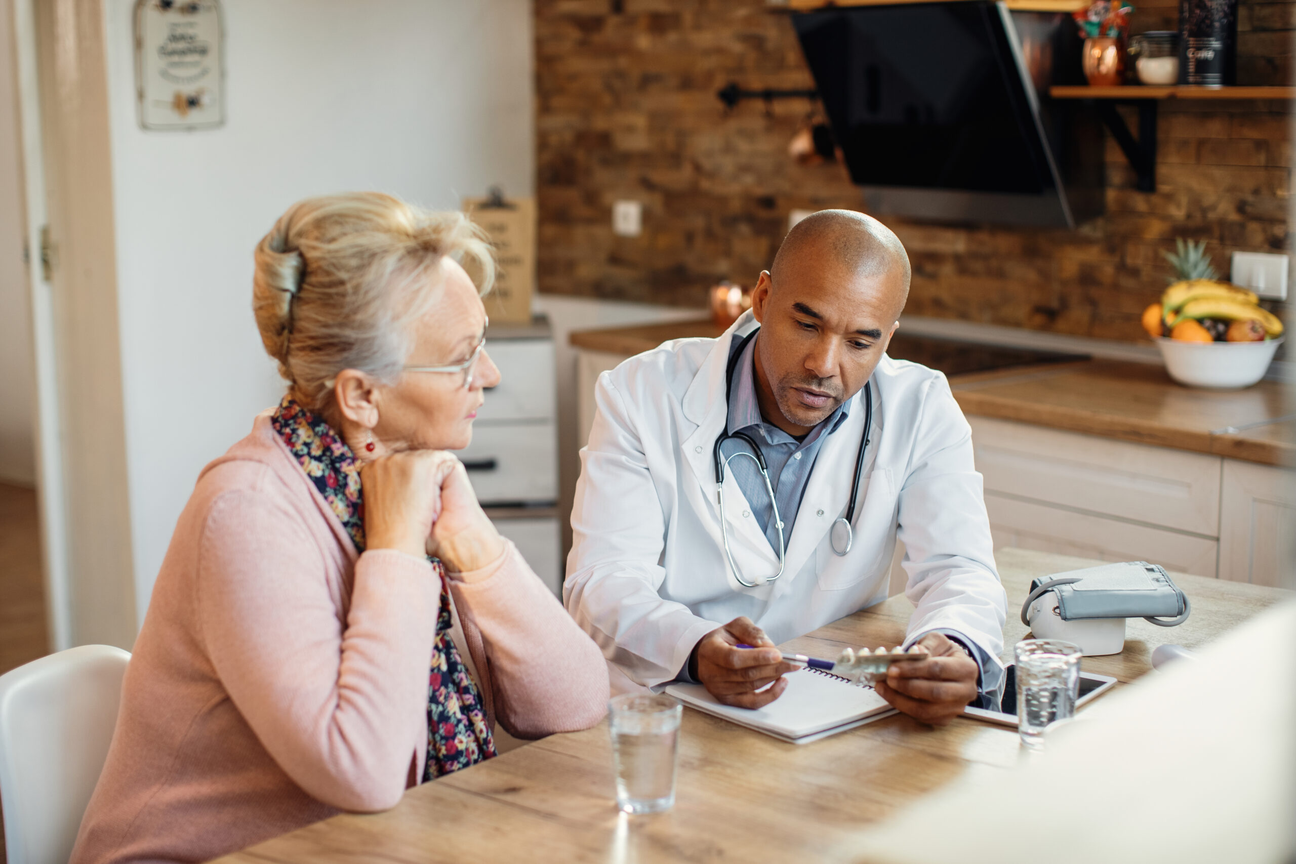 african american doctor talking about medicines with mature woman home visit scaled